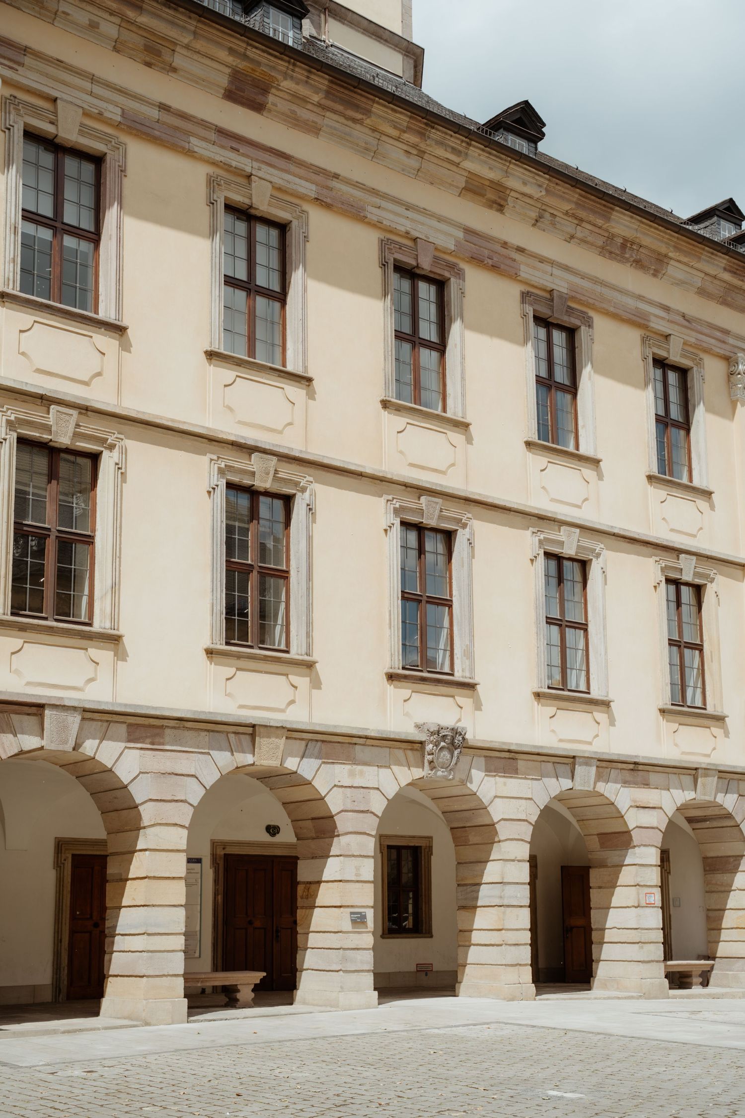 Historic building facade with arched colonnade and cream-colored walls featuring ornate architectural details and windows.