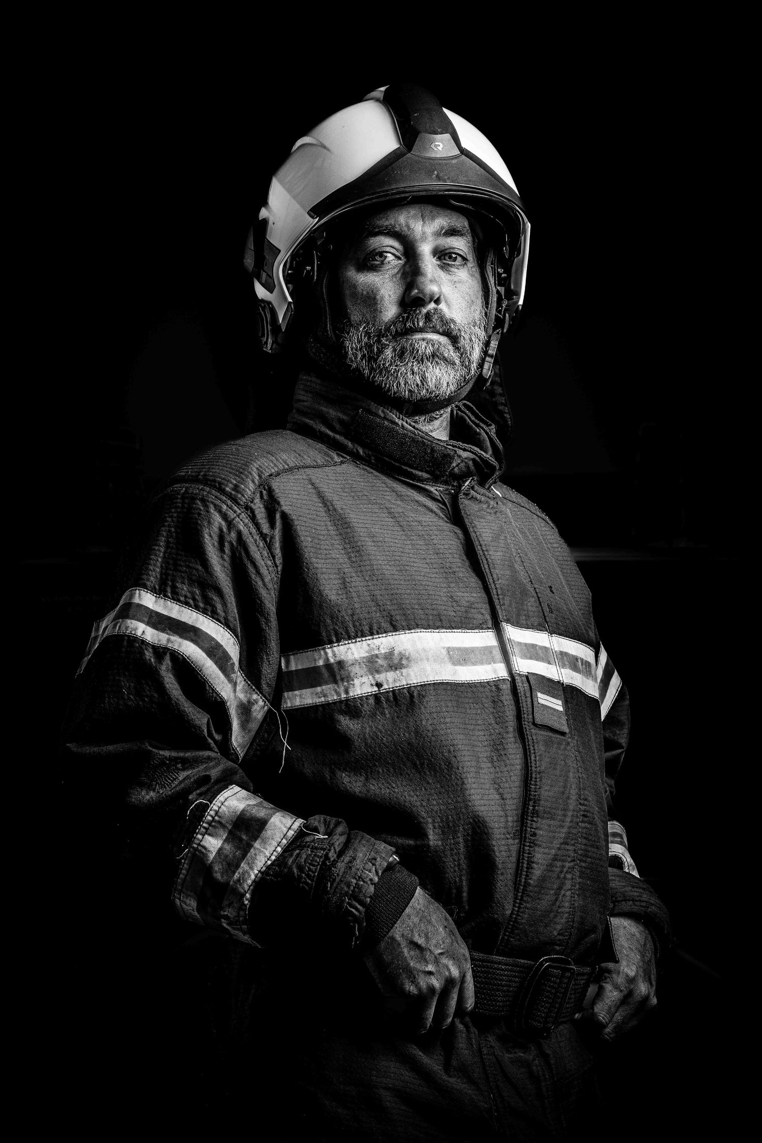 Black and white portrait of a bearded firefighter wearing helmet and reflective uniform.