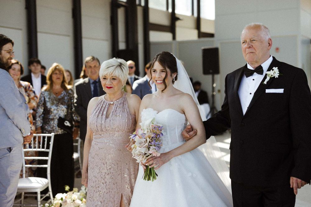 Wedding party poses in formal attire at an elegant indoor venue with white floral arrangements.