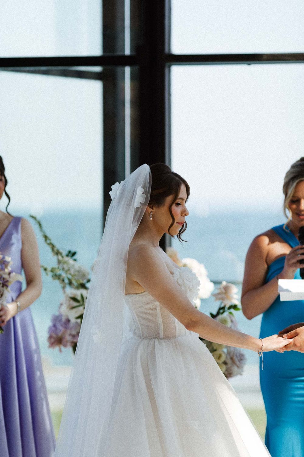 Bride in flowing white dress and veil dances in an elegant venue with large windows and ocean views.