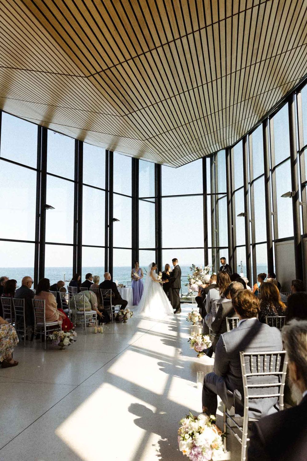 Modern event venue with floor-to-ceiling windows offering panoramic views and white chairs for seating.