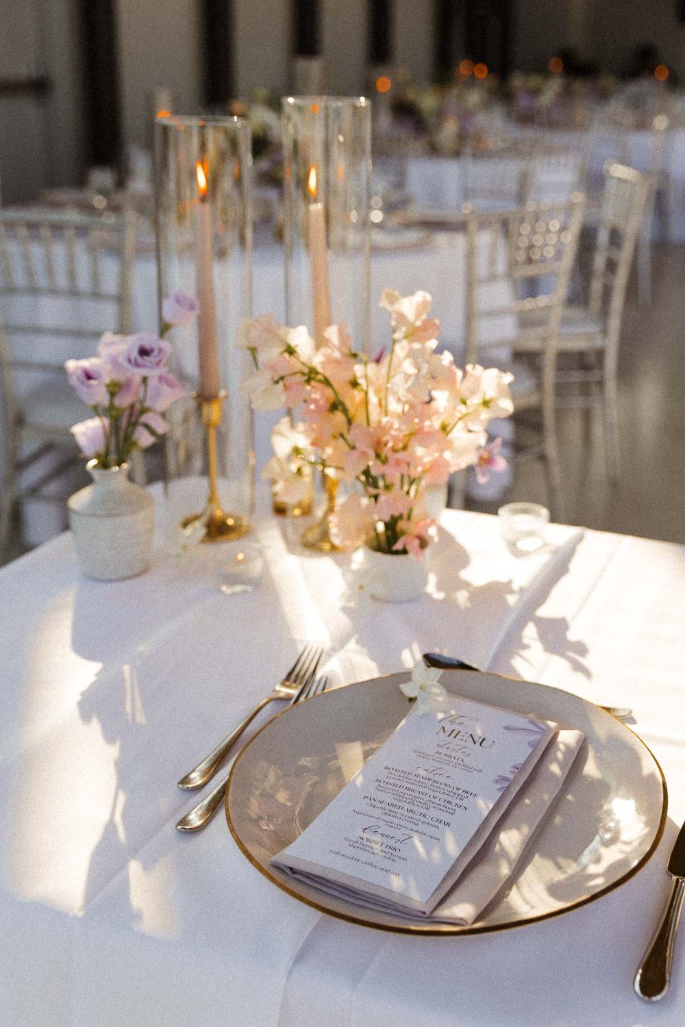 Wedding reception tables decorated with white linens, gold charger plates, and delicate floral arrangements.