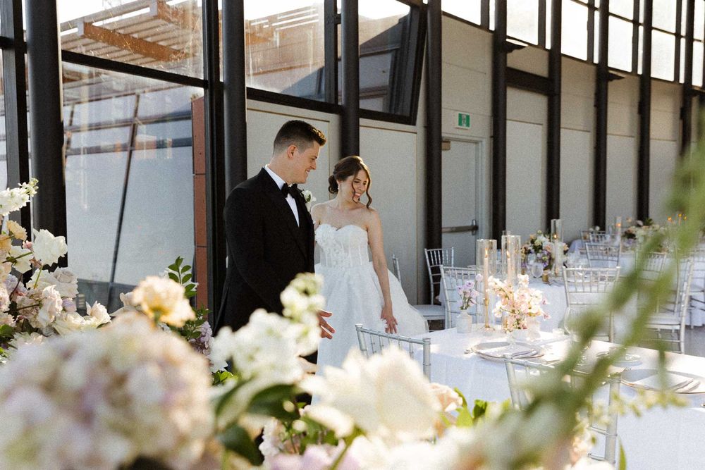 Elegant wedding reception table setting with floral centerpieces and natural light streaming through windows.