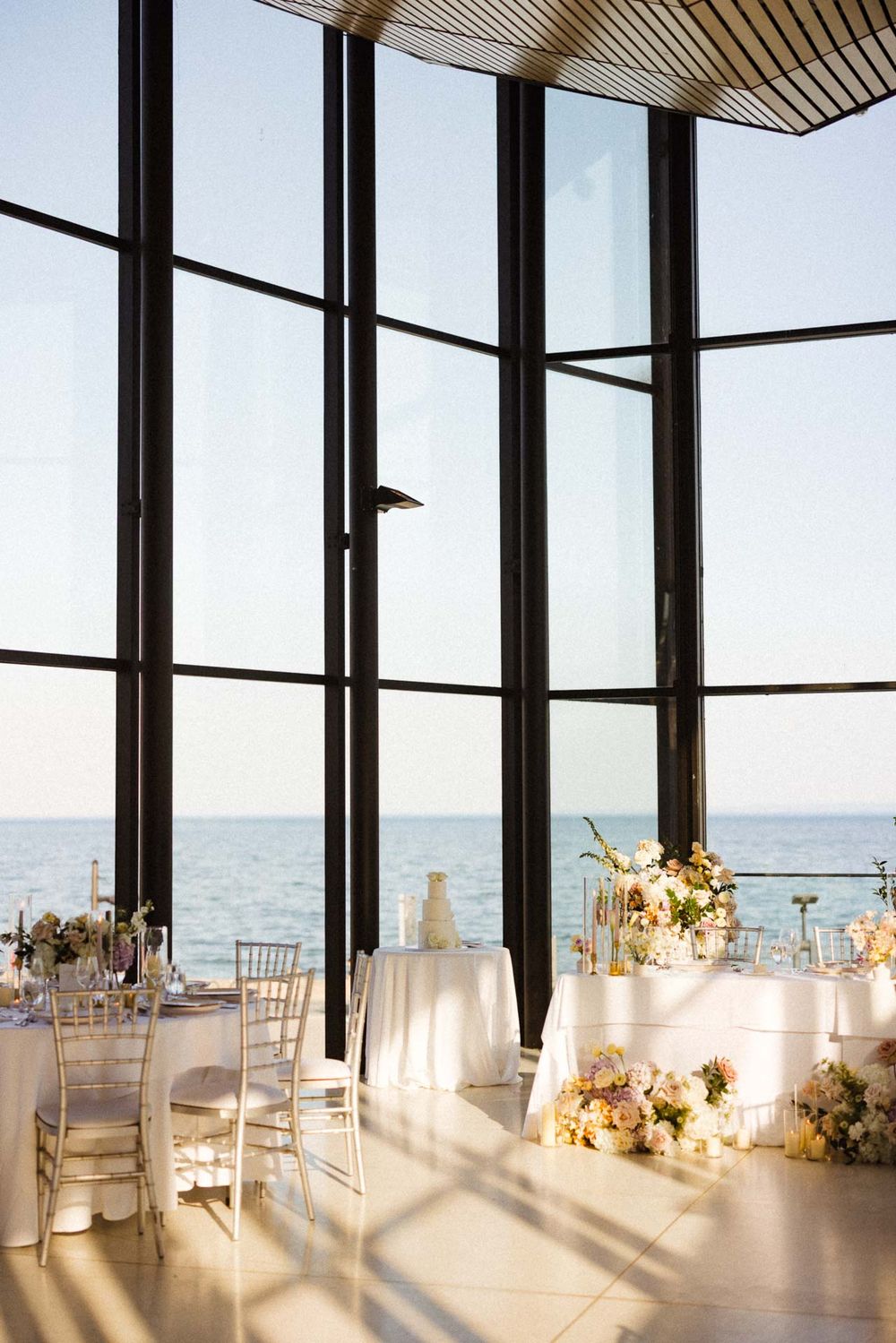 Modern waterfront wedding venue with floor-to-ceiling windows and white-decorated reception tables.