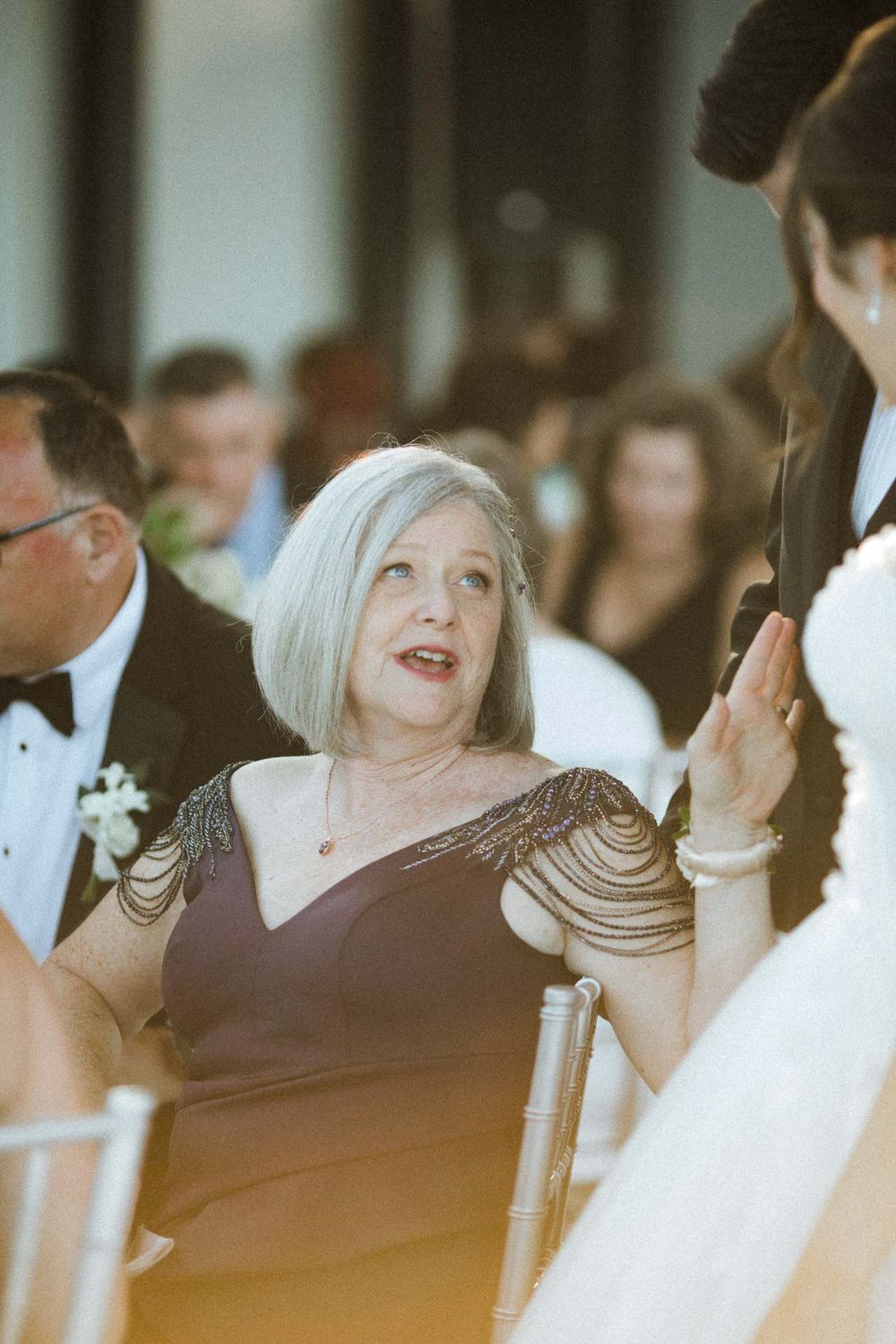 Wedding guests in formal attire laugh and smile during an indoor reception celebration.