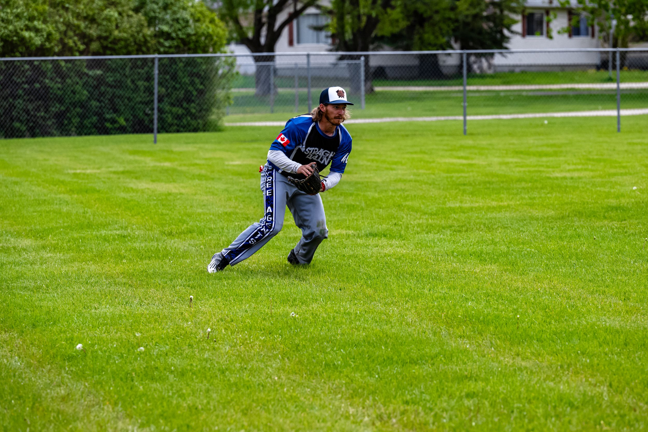 A person in blue and gray clothing plays baseball in a lush green field during a game.