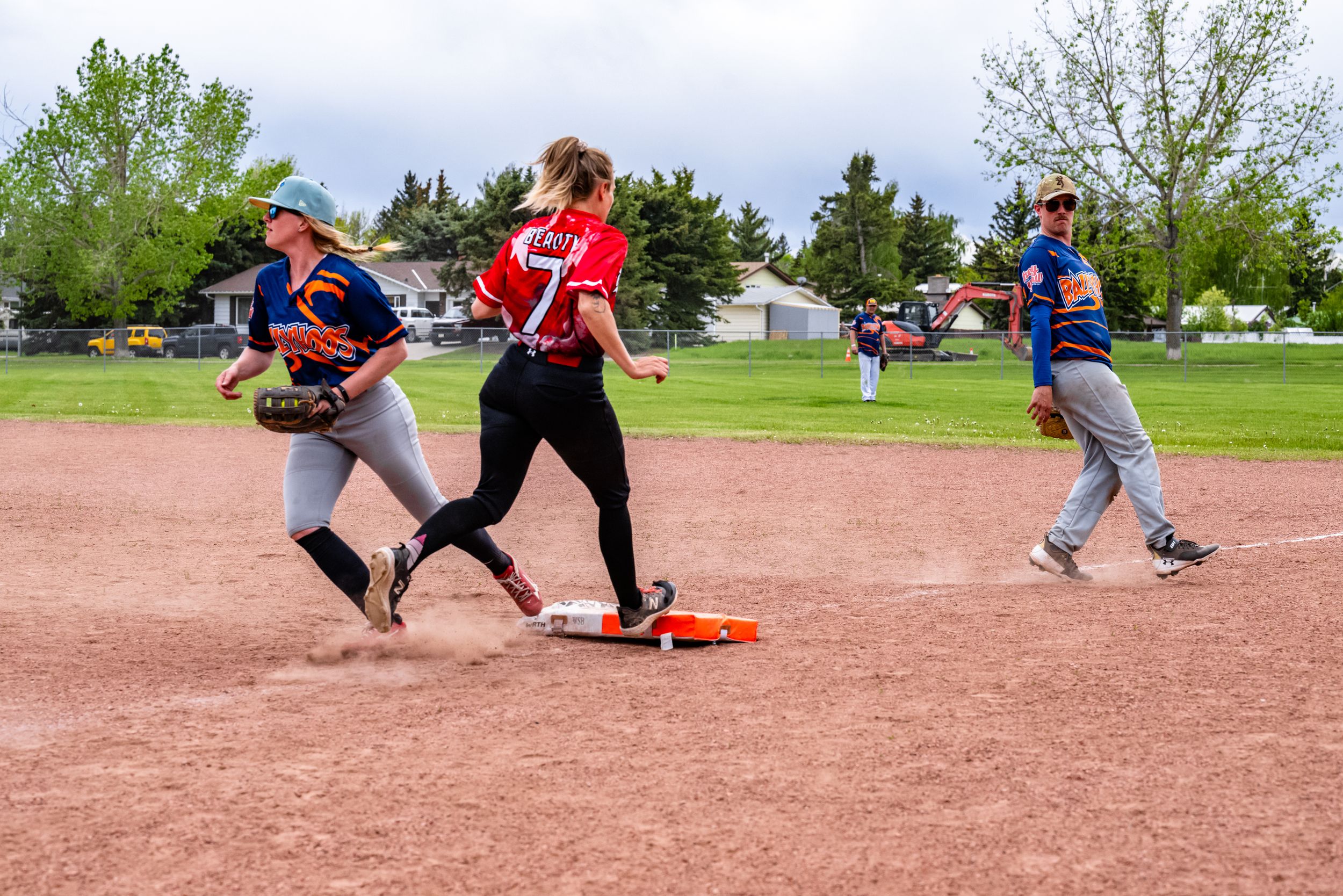 Softball players in action during a game with one runner touching first base while others move on the dirt infield.