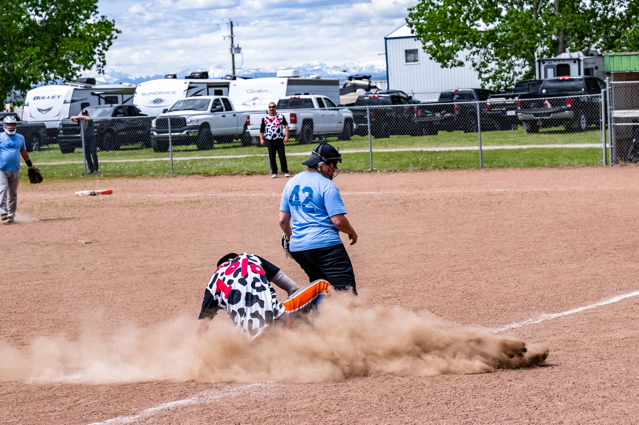 Baseball player slides into base creating a cloud of dust during an intense game on a dirt field.