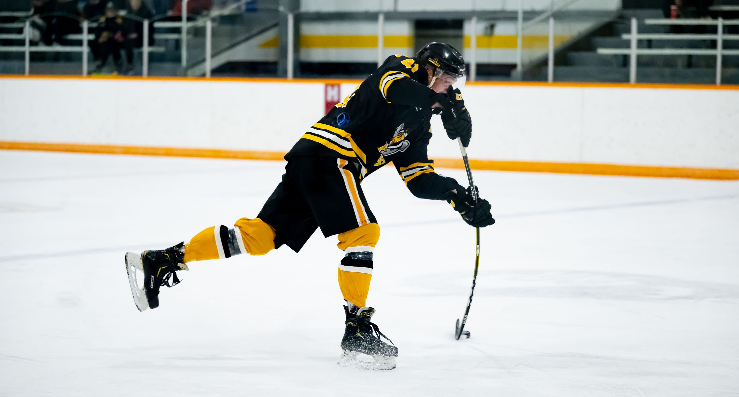 A hockey player in black and yellow uniform skates across the ice during a game.