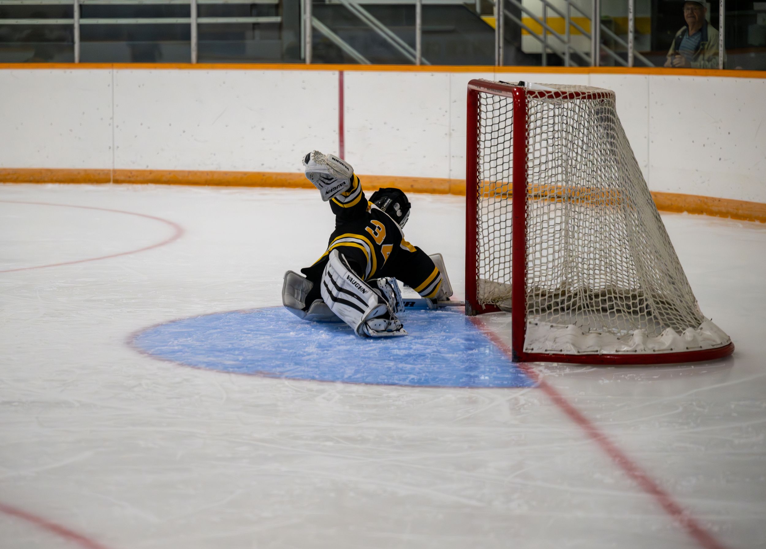 A hockey goalie stretches across an empty net on an ice rink during a game.