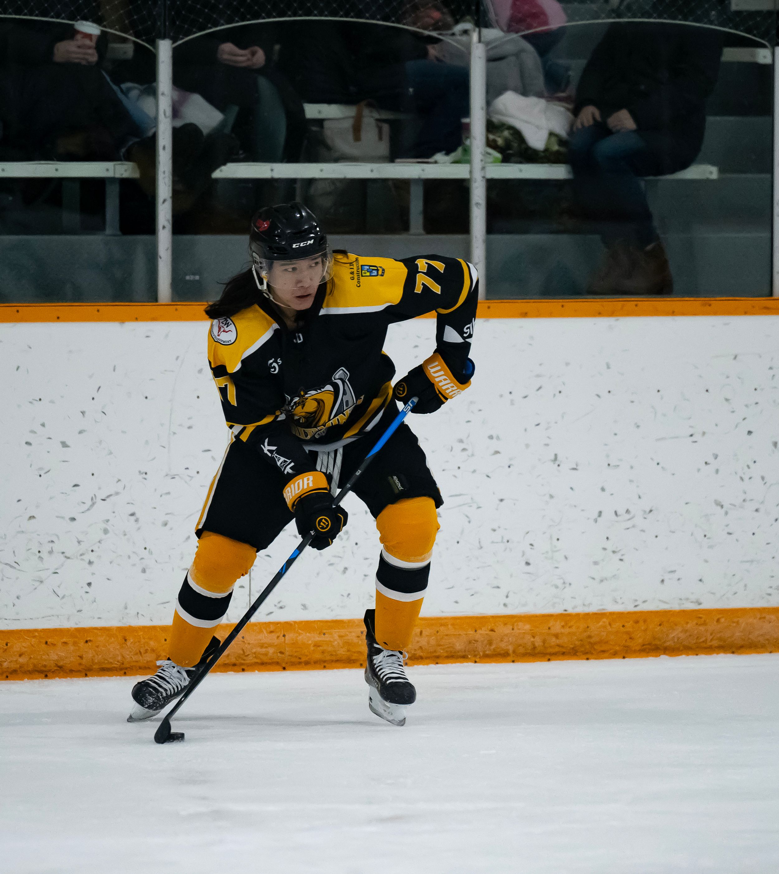 Hockey player in black and yellow jersey controls puck while skating on ice rink during game.