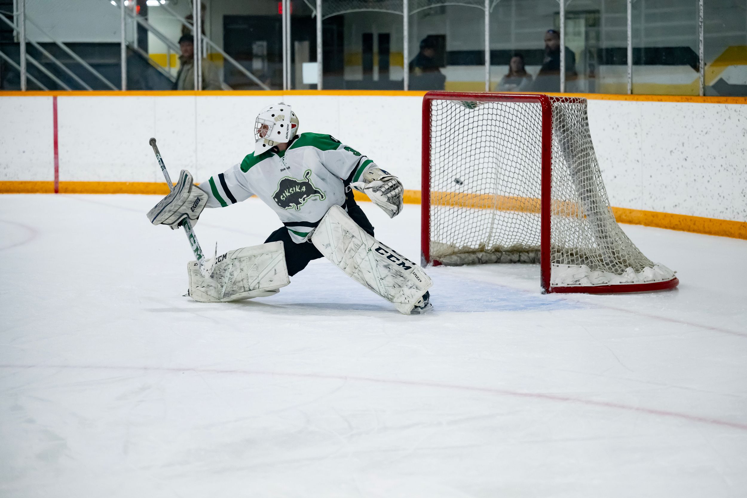 Hockey goalie makes a diving save attempt to block the puck during an intense game on the ice.