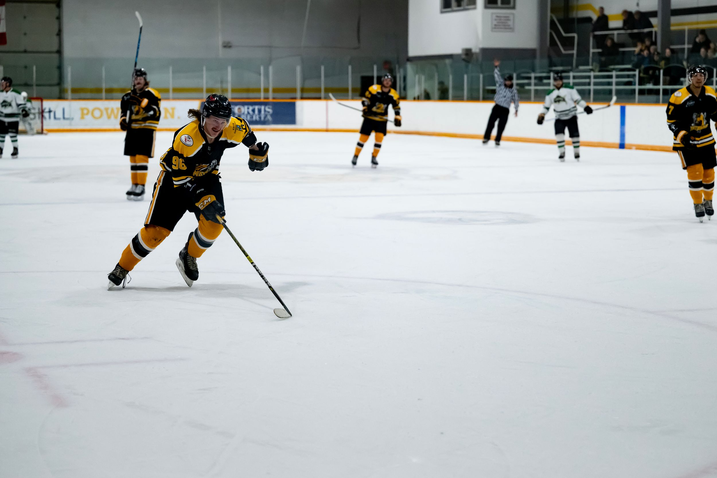 Ice hockey players in black and gold uniforms compete during a match on a brightly lit indoor rink.