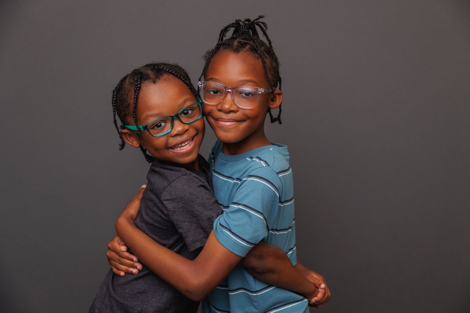Two children wearing glasses embrace and smile together in a heartwarming series of candid portrait photos.