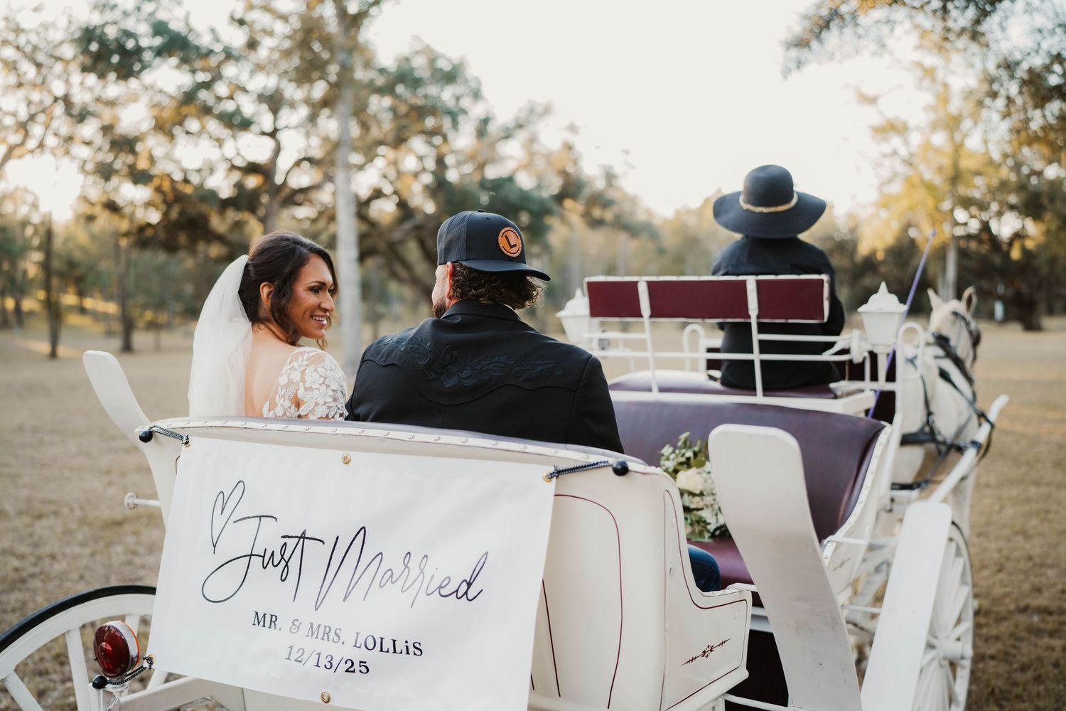 A vintage car decorated with wedding signage and floral arrangements parked outdoors at sunset.