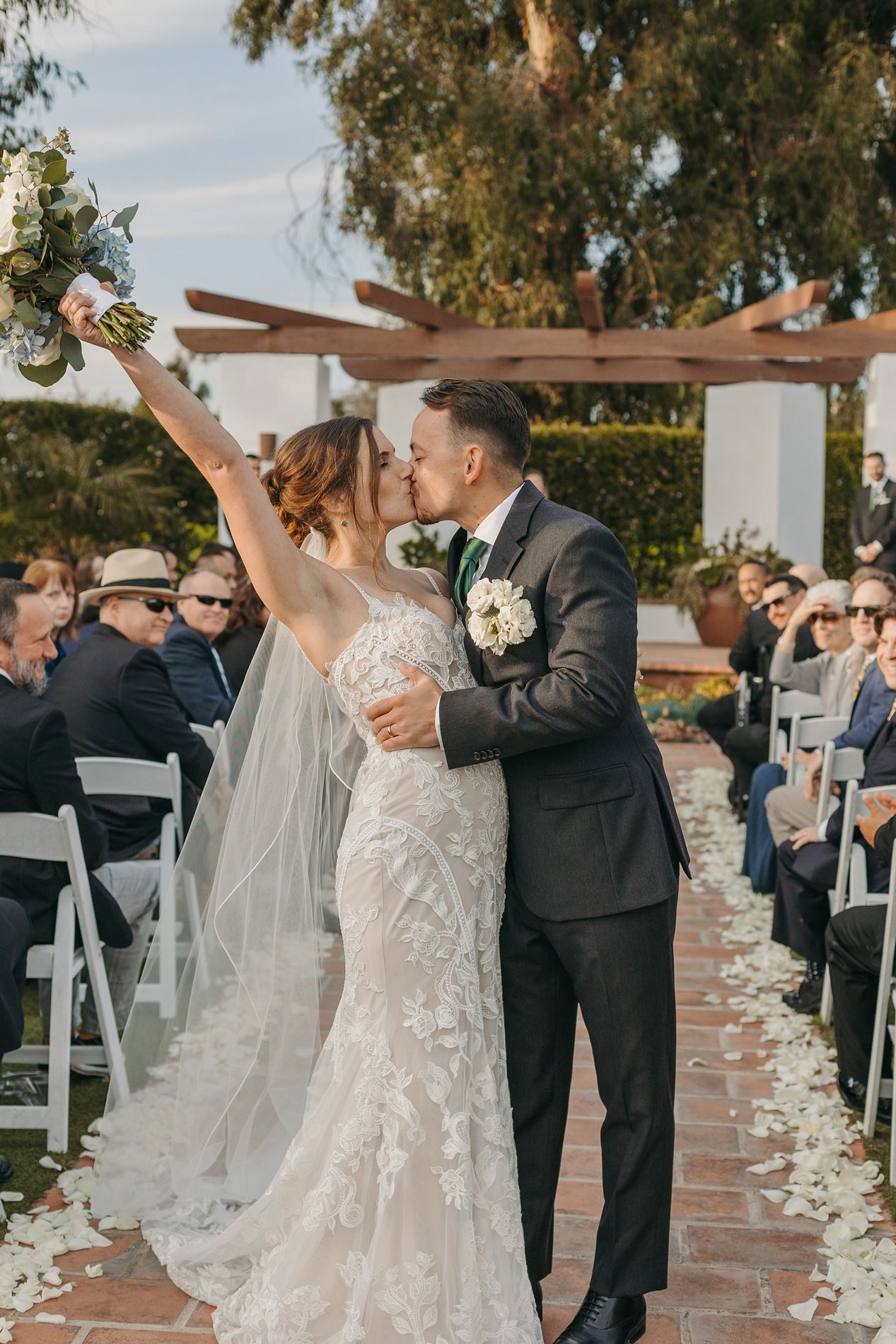 Newlyweds celebrates during outdoor wedding ceremony with white chairs and floral petals at San Clemente Shores.