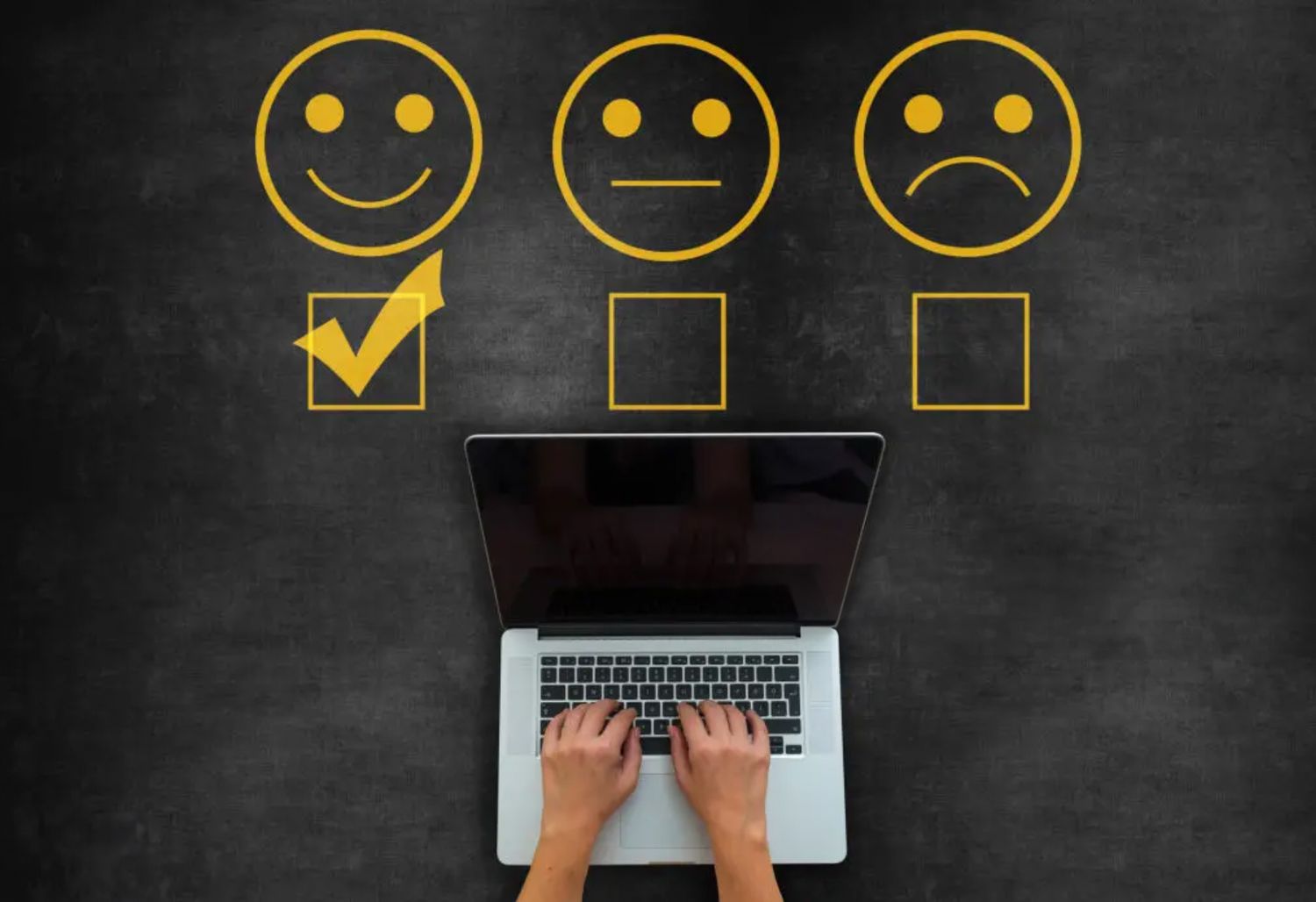 Person typing on laptop with three emoji faces drawn on chalkboard above showing customer satisfaction feedback options.
