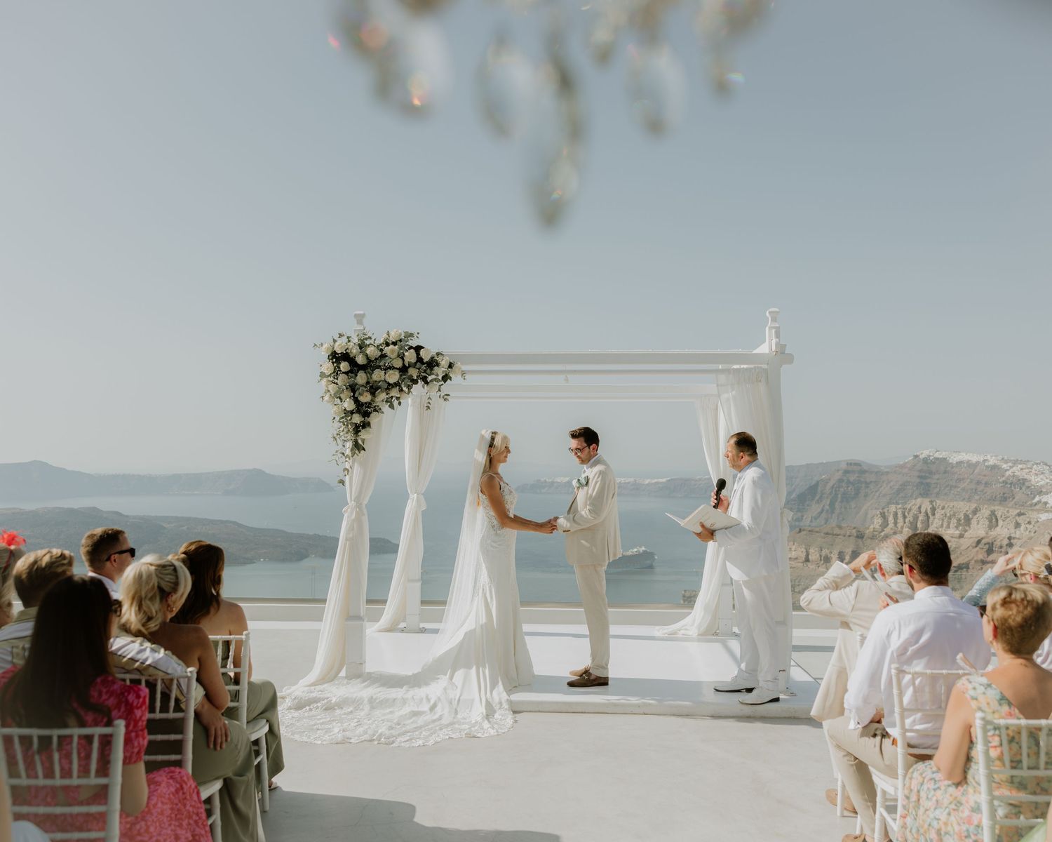 White chairs and floral arrangements line an outdoor wedding ceremony venue overlooking a scenic ocean view.