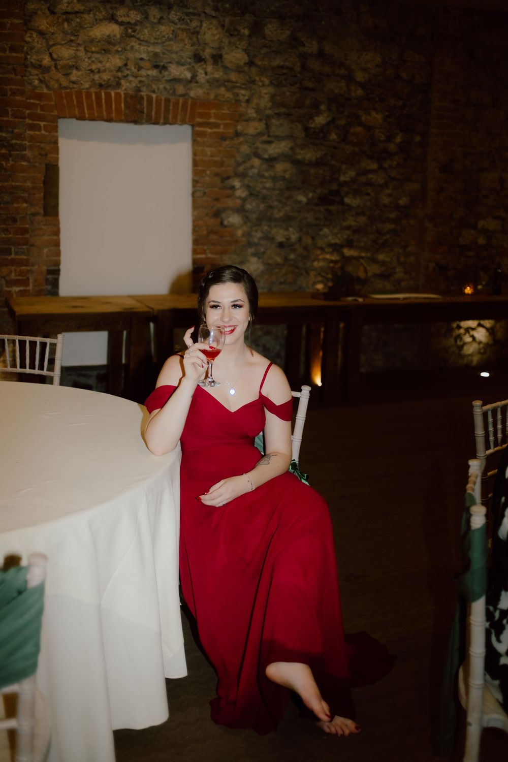 A sequence of photos showing a person in a red dress posing playfully at a rustic stone-walled venue with white tables.