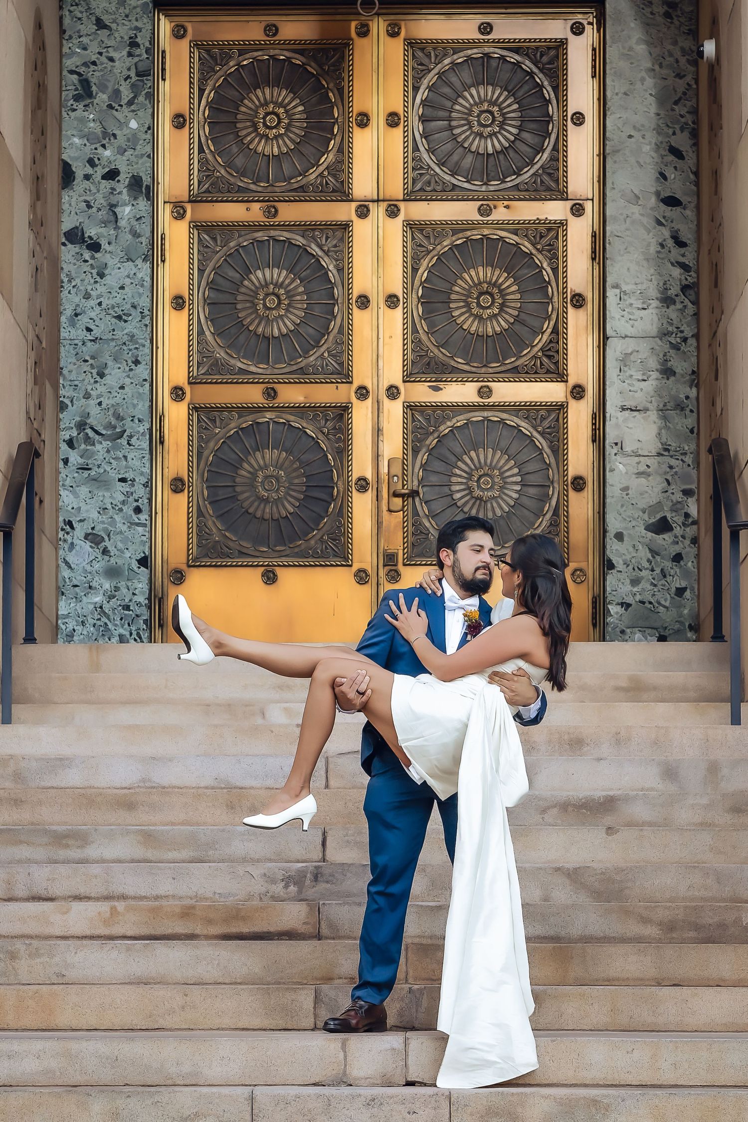 A romantic dip pose in front of ornate gold and black doors on stone steps in downtown Phoenix Ariziona