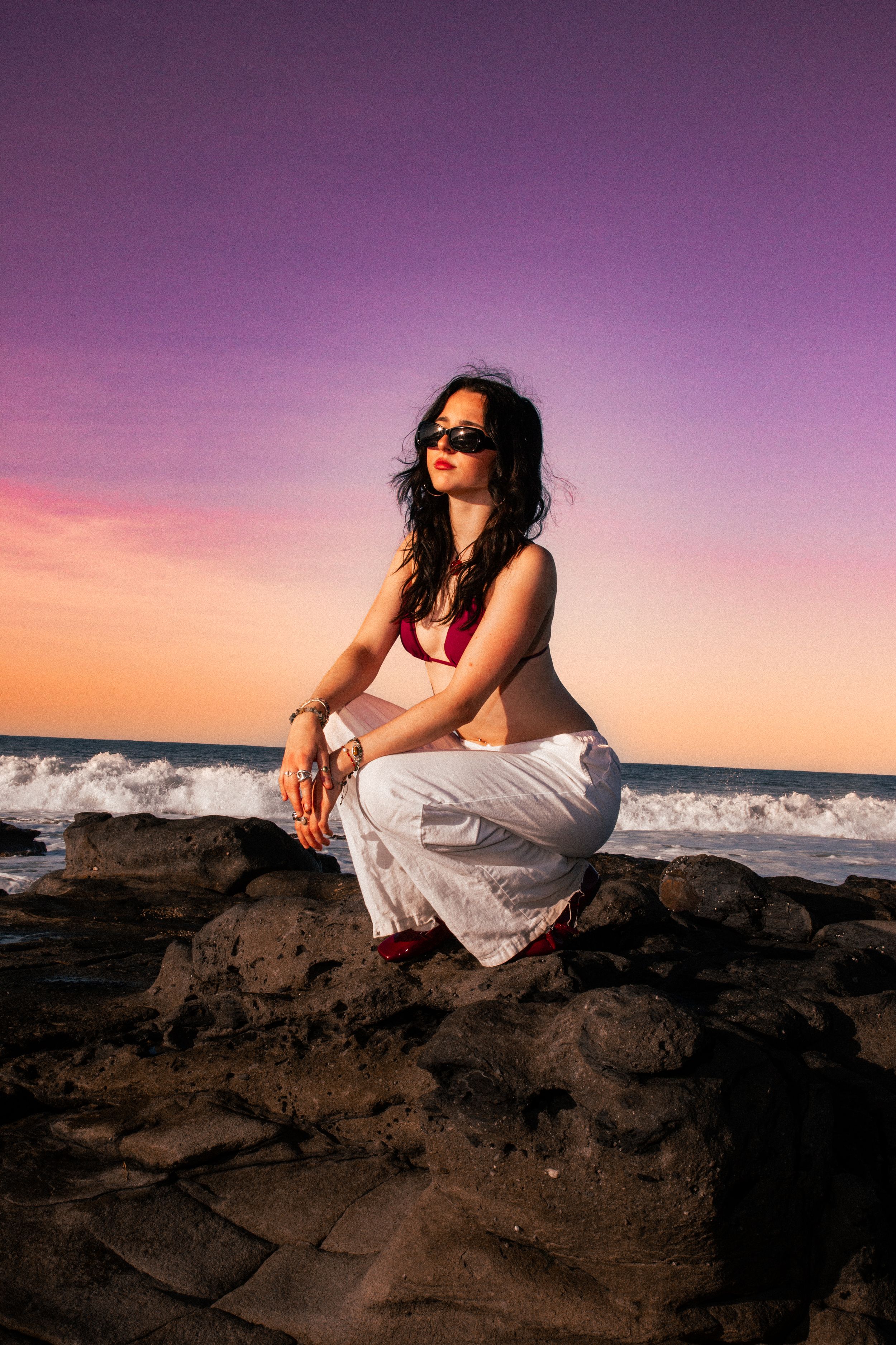 Fashion photography on rocky beach during vibrant purple sunset.