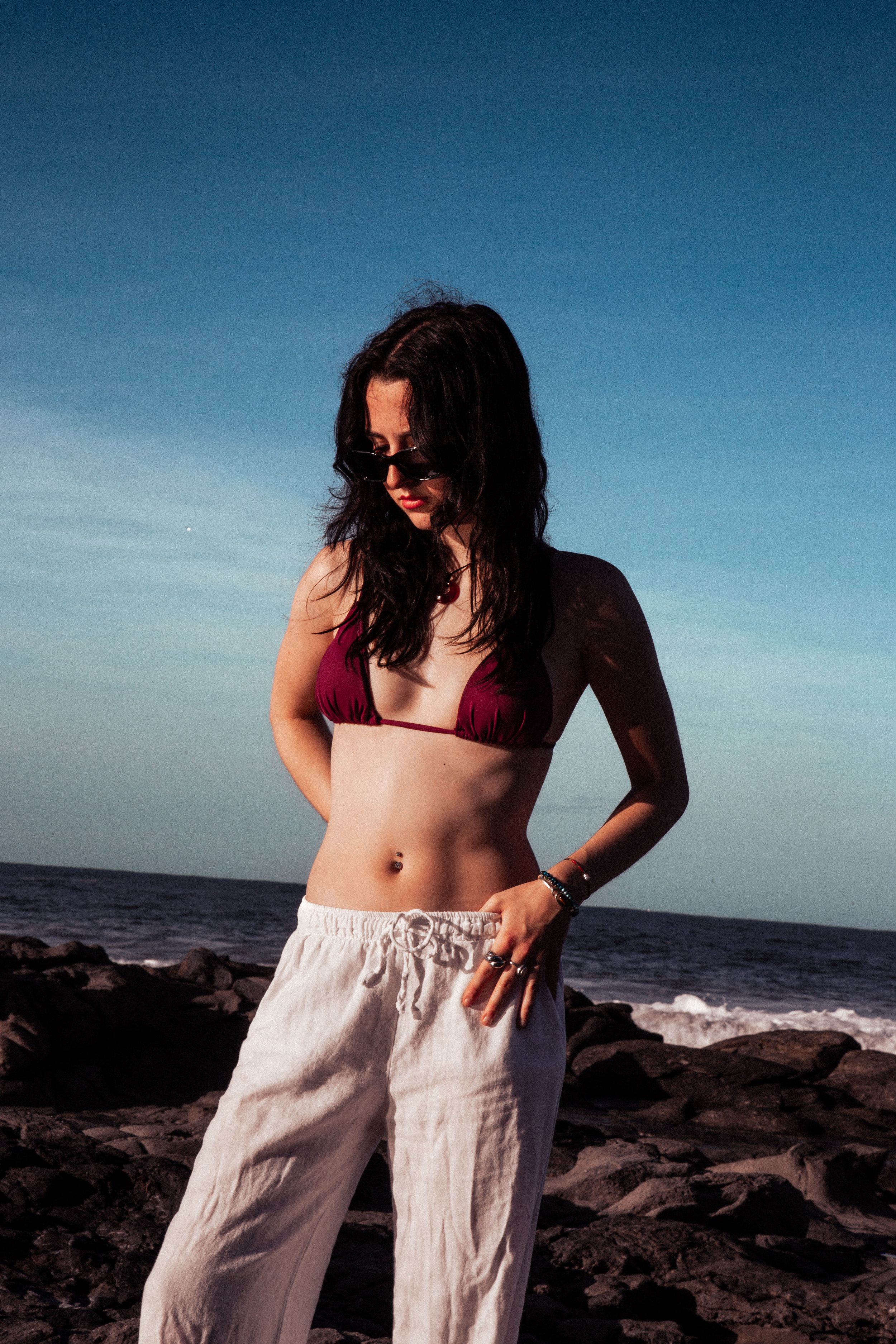 Casual beachwear fashion shoot on rocky coastline with blue sky backdrop.