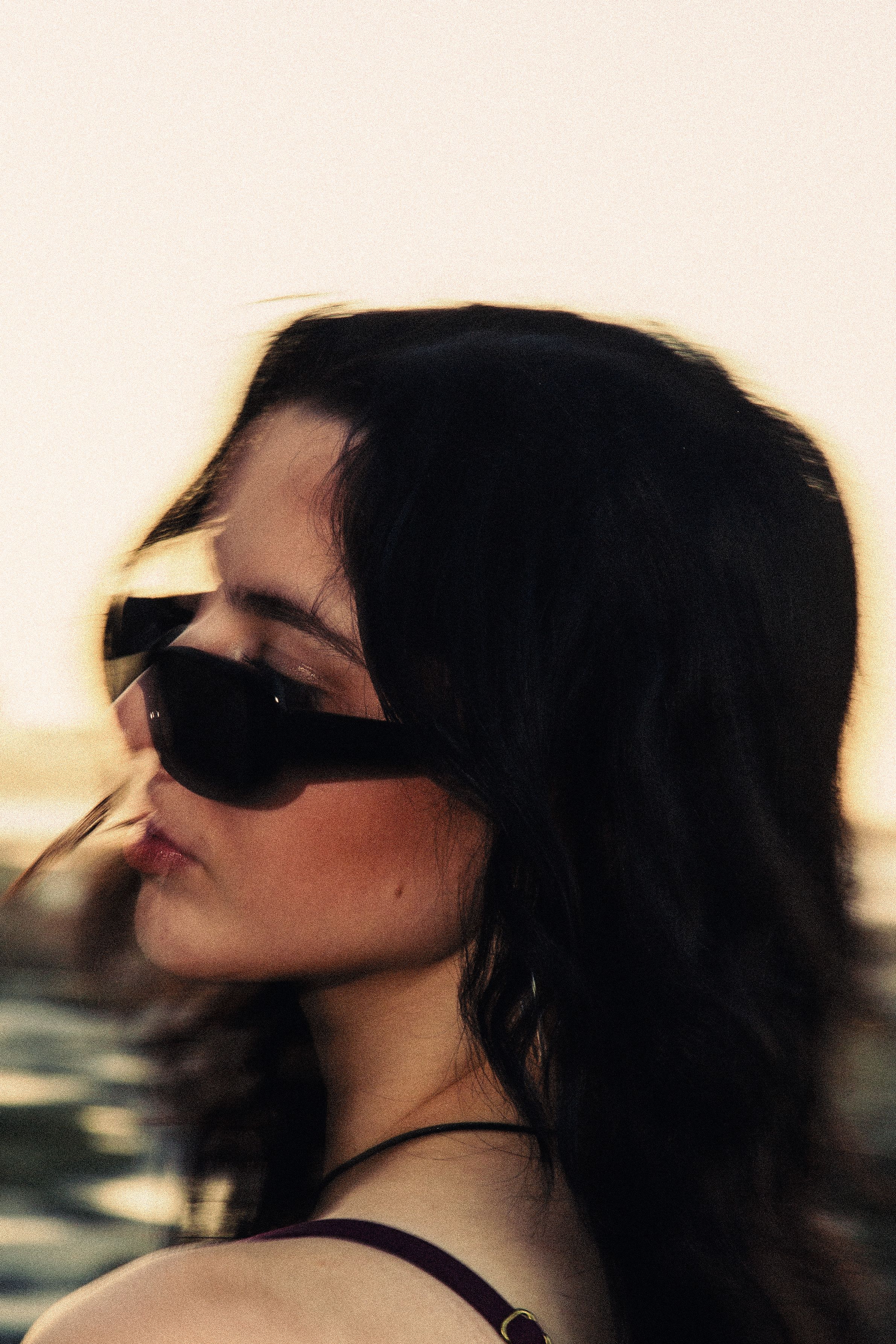 Artistic close-up portrait with sunglasses during golden hour at beach.