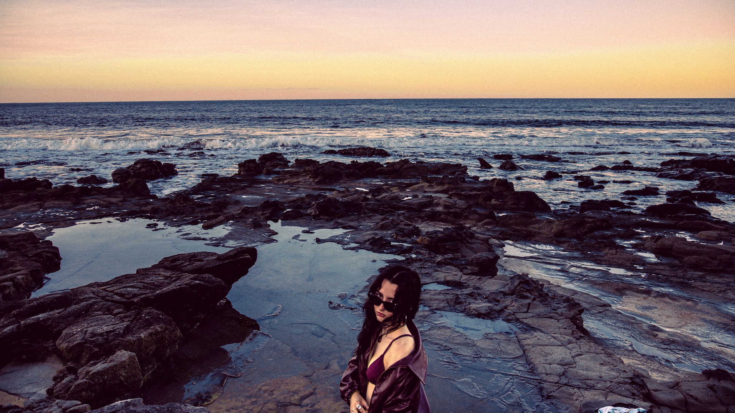 Seaside sunset view with rocky shore and ocean waves.