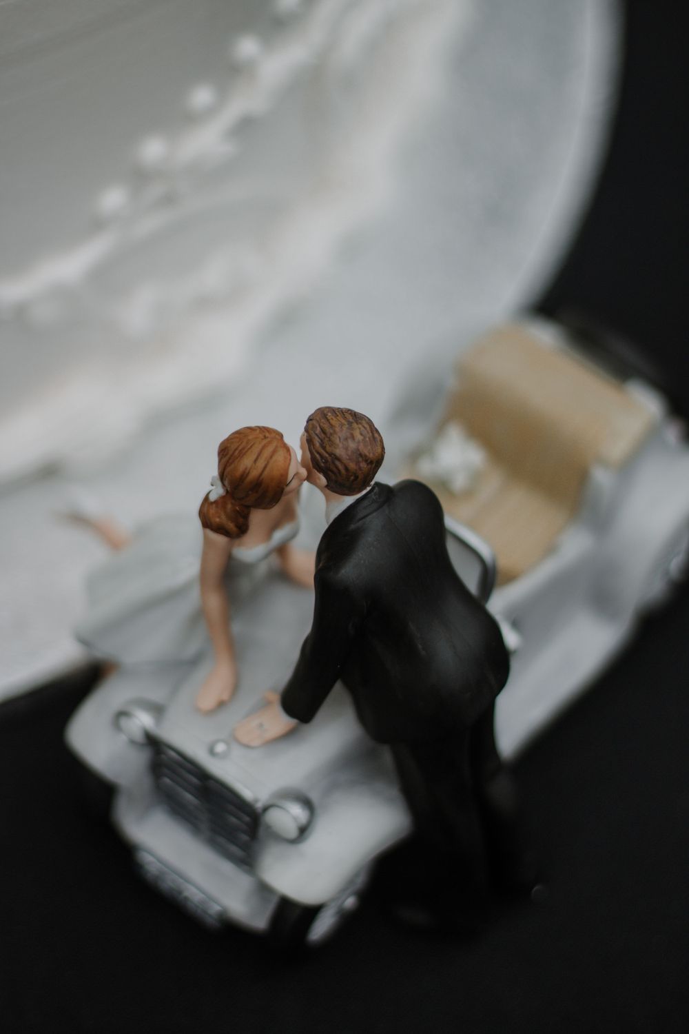 Close-up of wedding cake topper with bride and groom figurines leaning in for a kiss.
