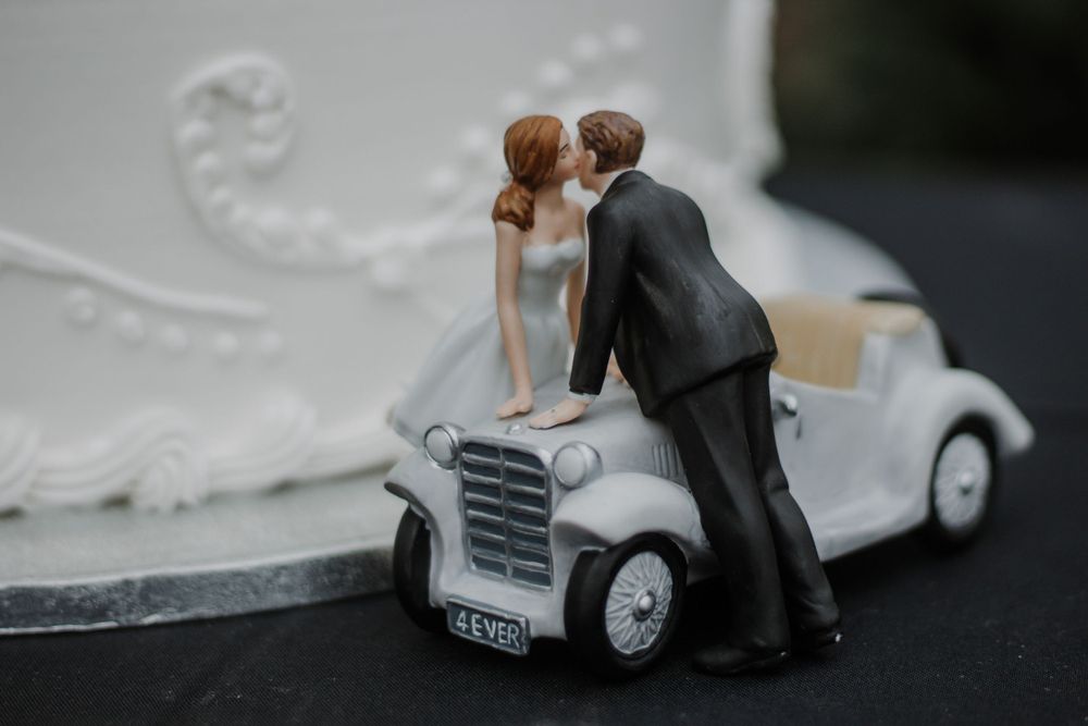 Elegant wedding cake topper featuring bride and groom figurines kissing over a vintage car.