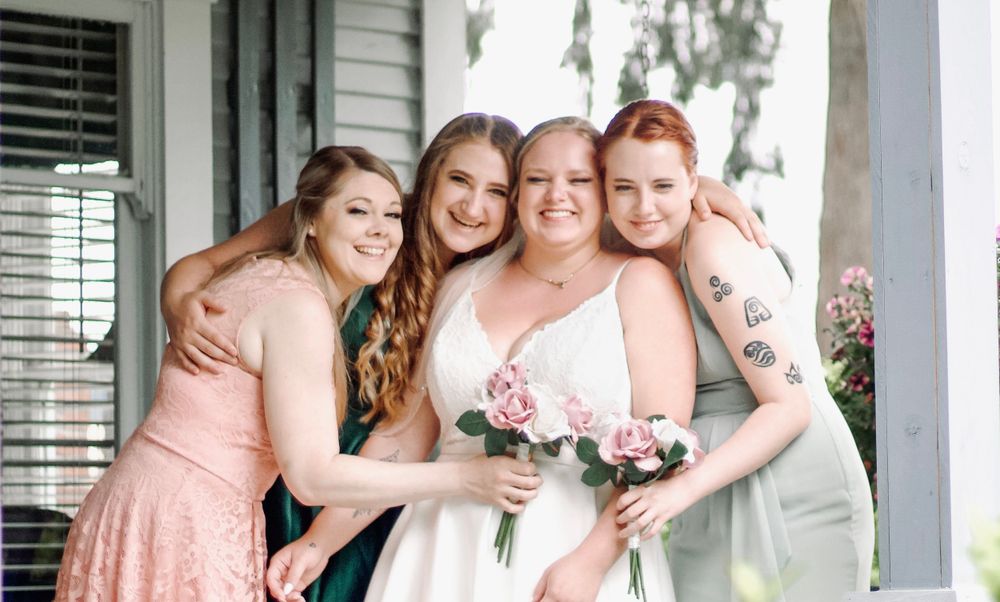 Bride smiling with three bridesmaids in colorful dresses holding a pink bouquet.