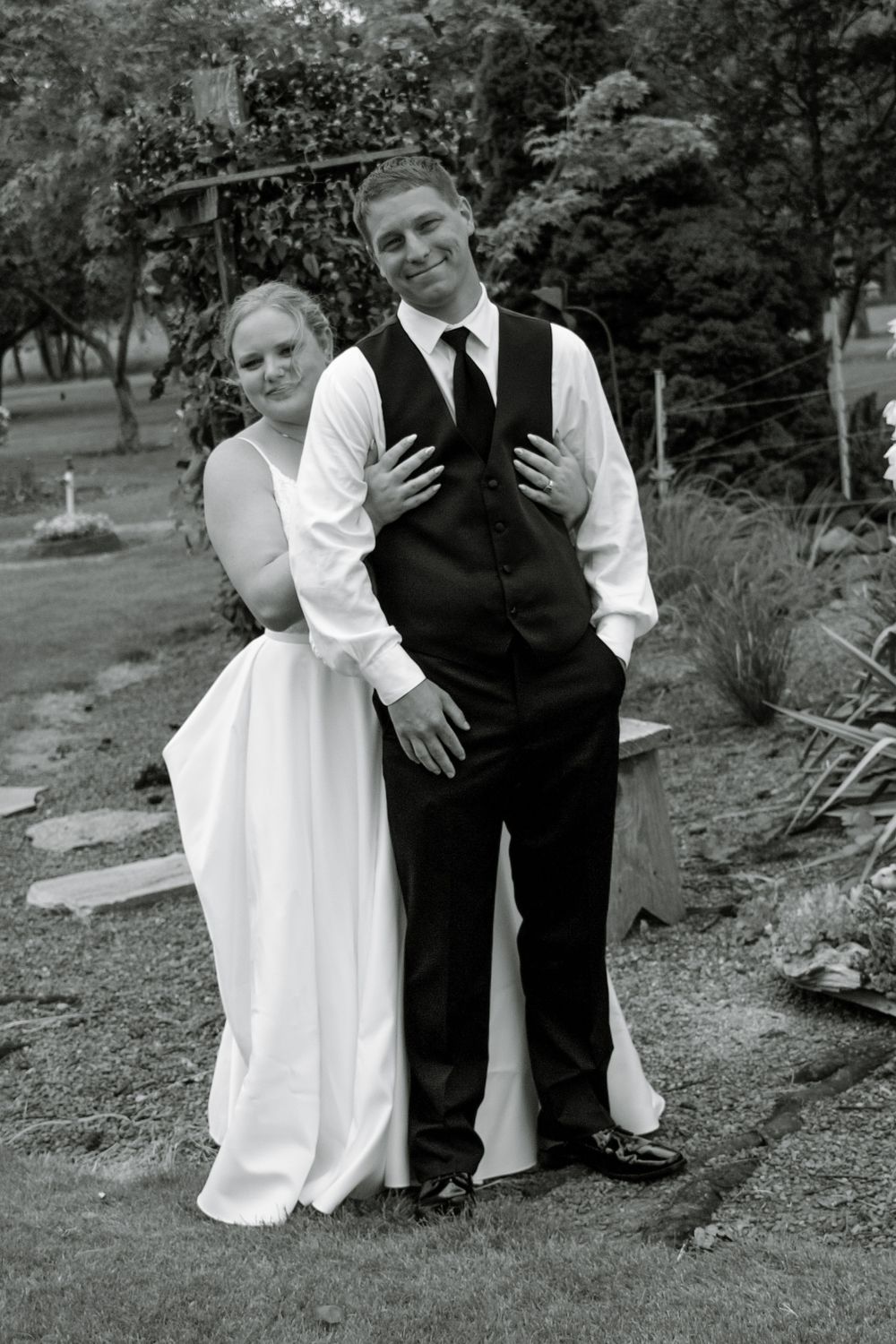 Black and white photo of bride and groom posing together outdoors at their wedding.