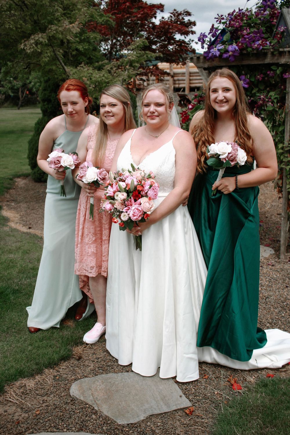 Bride in white gown poses with three bridesmaids holding pink bouquets in a garden.