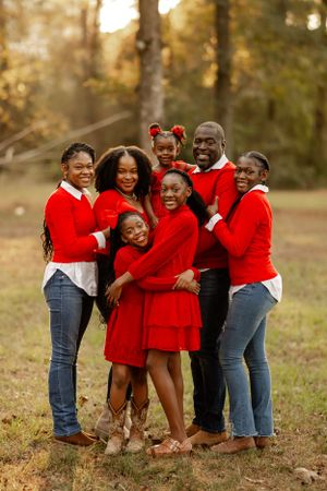 A joyful group wearing coordinated red sweaters poses together outdoors during golden hour in an autumn forest setting.