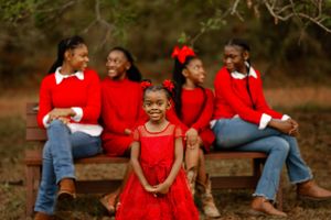 A group of people in bright red sweaters and jeans sit and laugh together on a wooden bench outdoors.