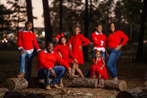 A family wearing matching red outfits poses outdoors in a natural setting with trees during golden hour.
