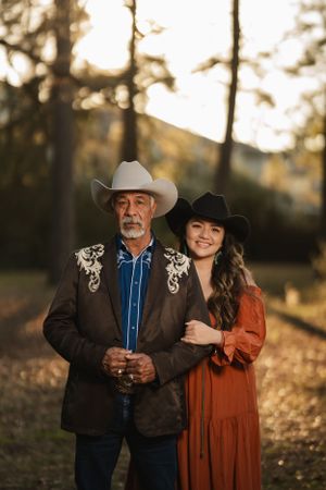 A western-styled portrait of two people in cowboy hats standing together in a forest at golden hour.