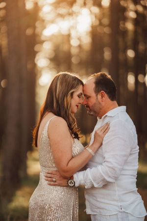 A romantic sunset engagement photo showing a couple embracing in a forest with golden bokeh lighting in the background.