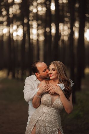 A romantic moment captured in a forest with soft bokeh lighting at sunset, featuring an intimate embrace in evening attire.