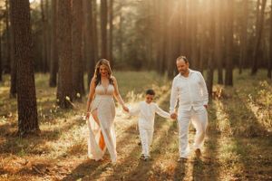 A family holding hands walks together through a sunlit forest clearing at golden hour.