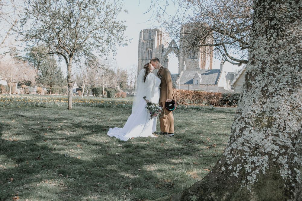 A couple poses romantically on a grassy lawn with a historic stone church building in the background.