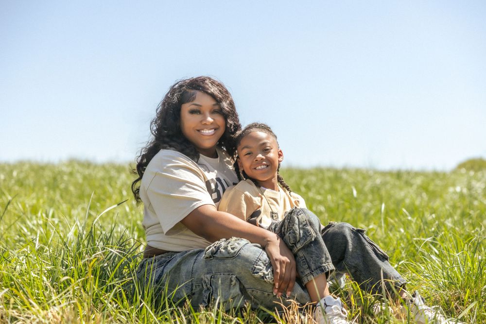 Two people sit together in a sunny meadow filled with tall grass on a bright spring day.
