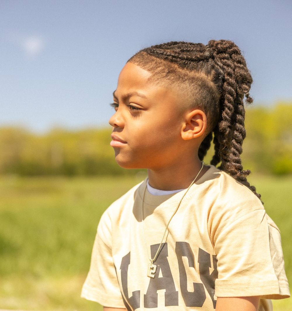 Young student in yellow Peace t-shirt with braided hairstyle gazes thoughtfully in sunny outdoor setting.