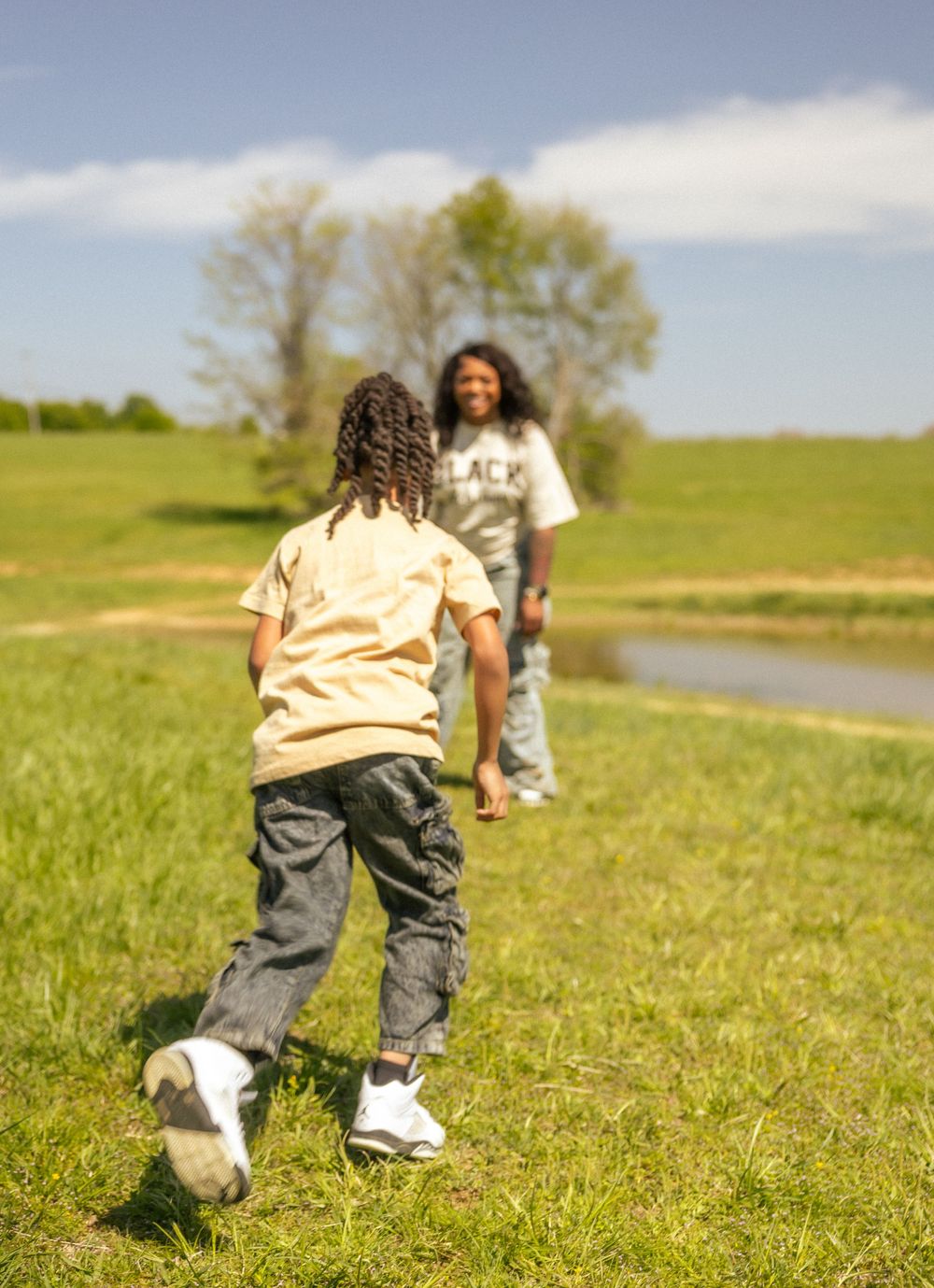 Two people spending time together on a grassy path near a stream on a sunny spring day.