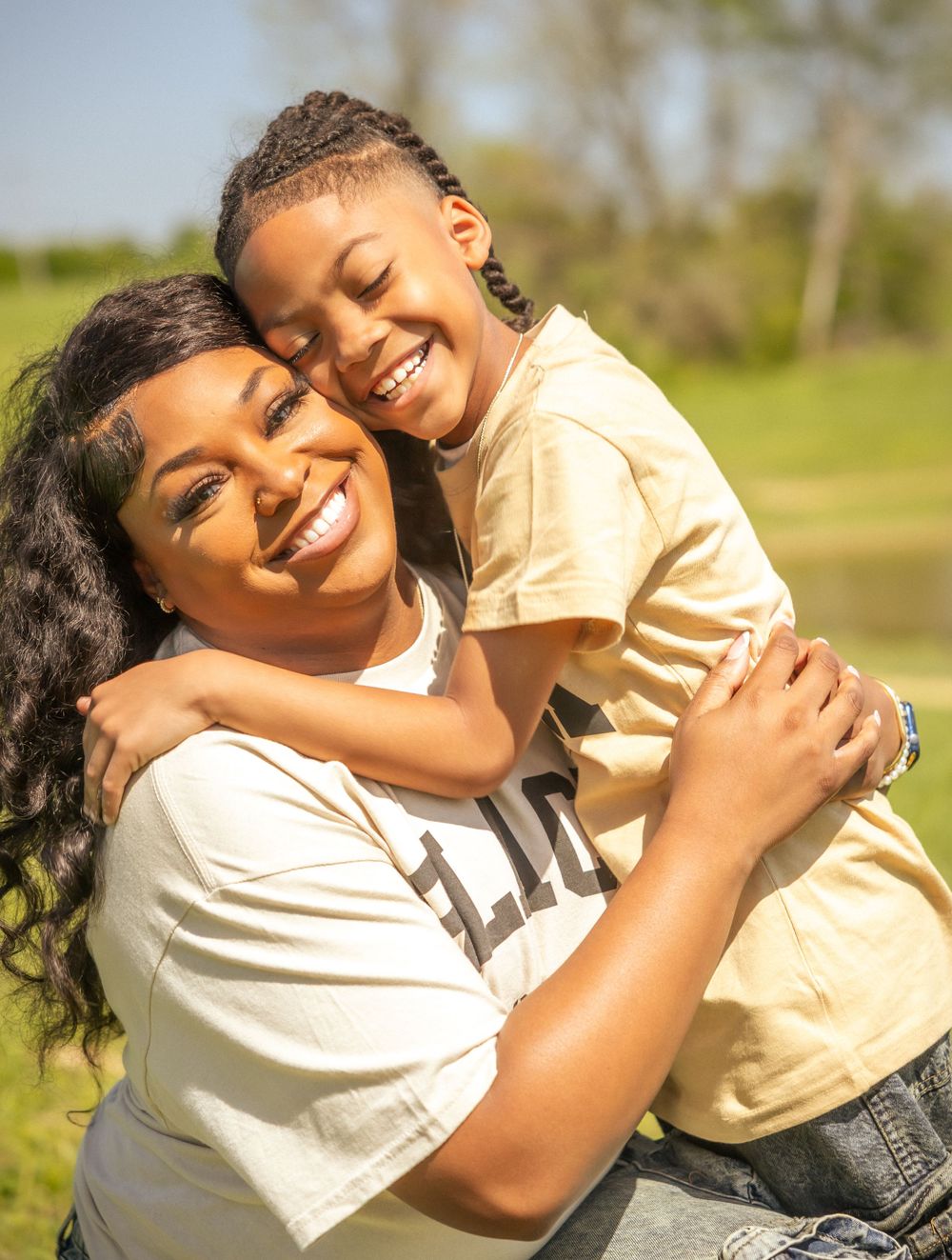 Two people share a joyful embrace while smiling outdoors on a sunny day in a grassy field.