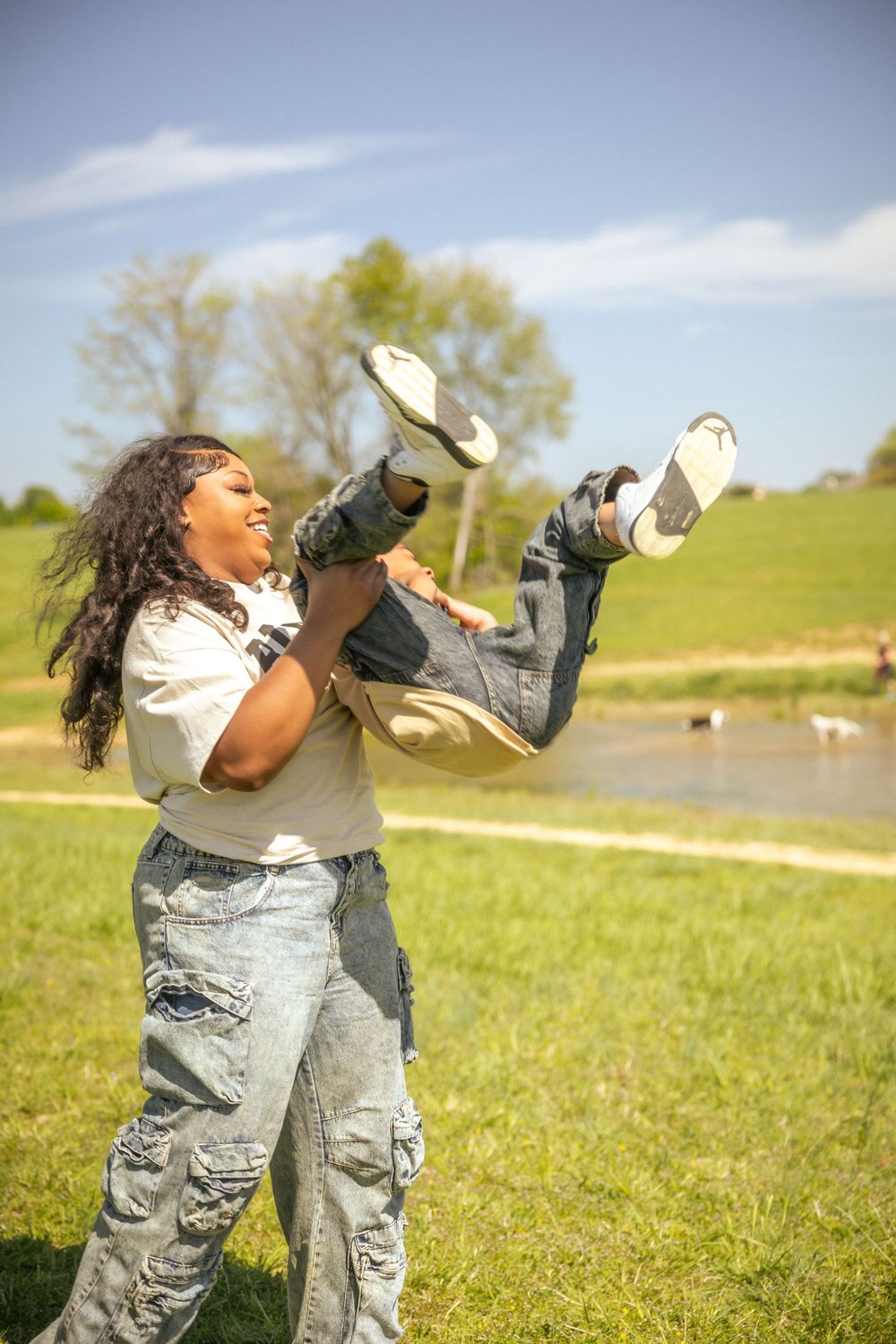 Person in casual attire playing outdoors in a grassy field on a sunny day, kicking their feet up playfully.