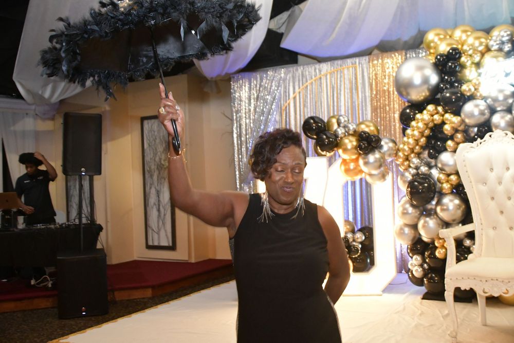 A person dancing under decorative black feathers near a balloon arch and white throne chair.