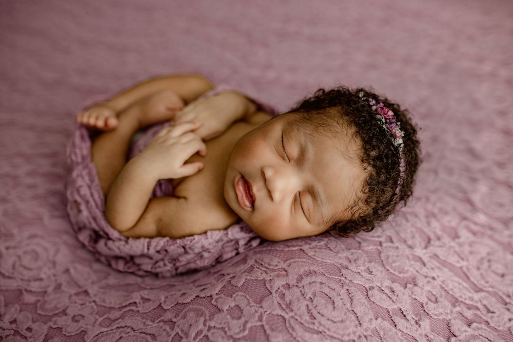 A peaceful sleeping newborn in a delicate pink lace blanket wearing a floral headband.
