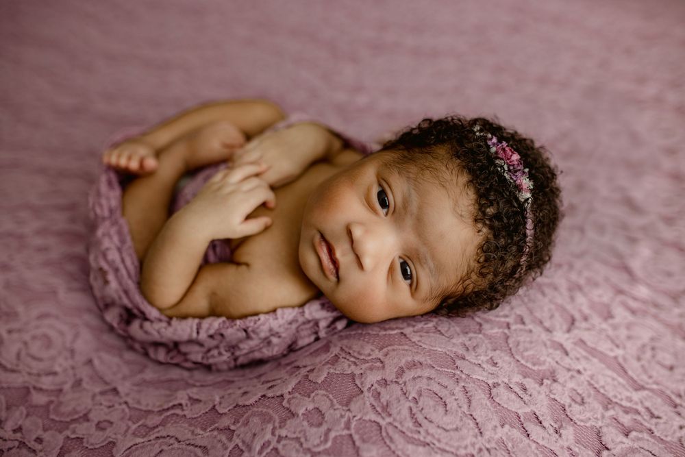 Baby wrapped in soft pink blanket lying on textured pink fabric during newborn photo session.
