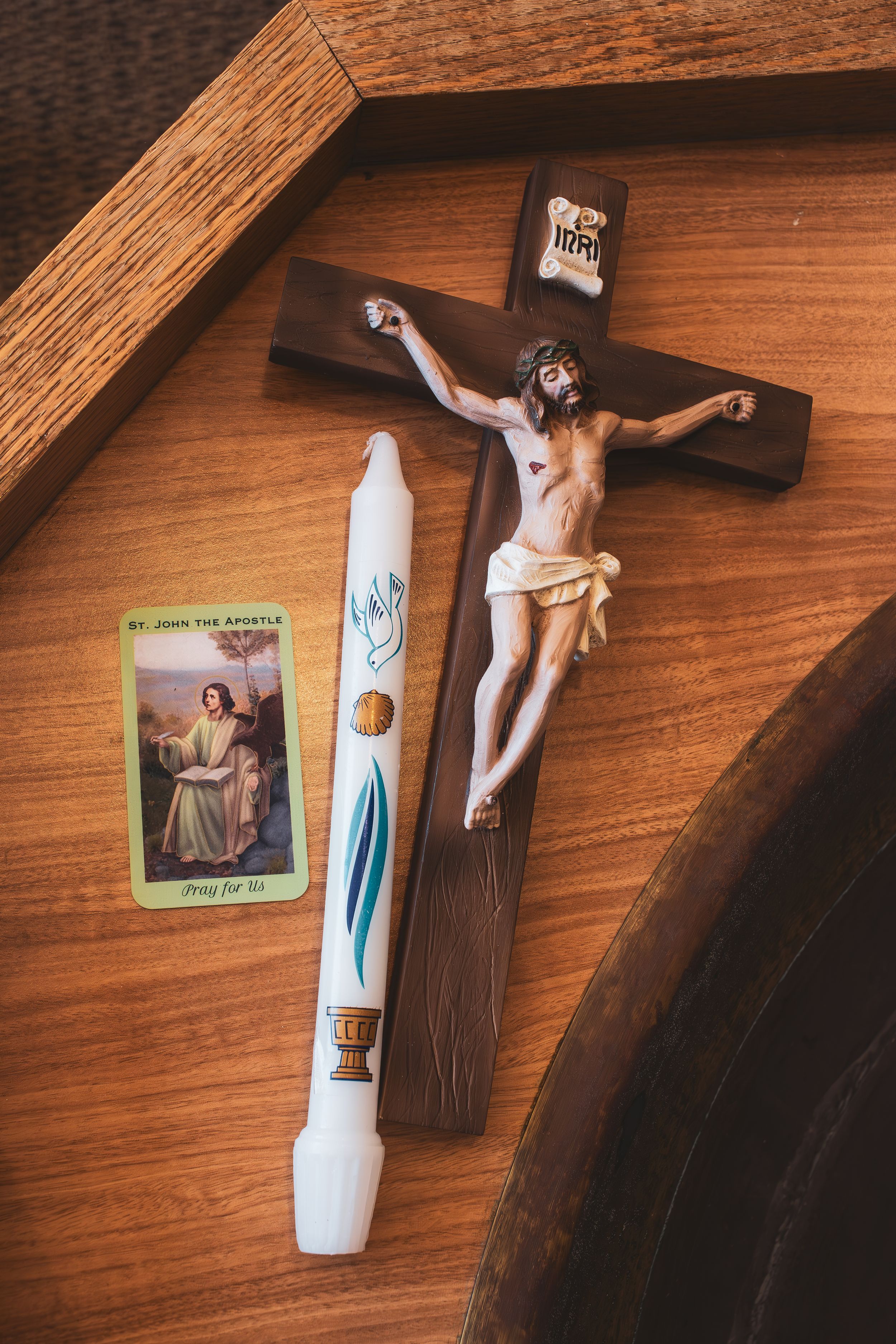 Religious items including a crucifix, prayer card, and white ceremonial candle on wooden surface.